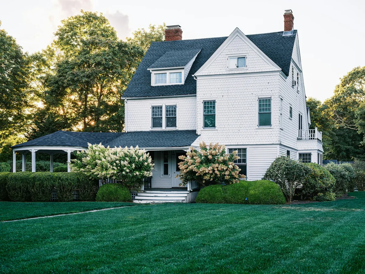 White two-story house with dark roof, landscaped garden and manicured lawn